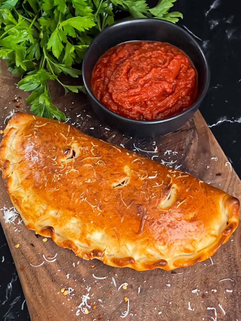 A calzone on a cutting board with a dipping sauce.