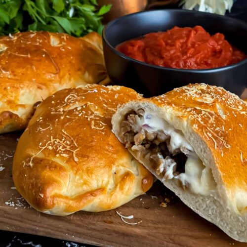 A calzone on a cutting board with a dipping sauce.