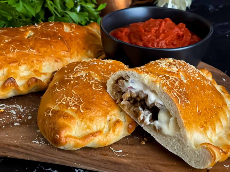 A calzone on a cutting board with a dipping sauce.