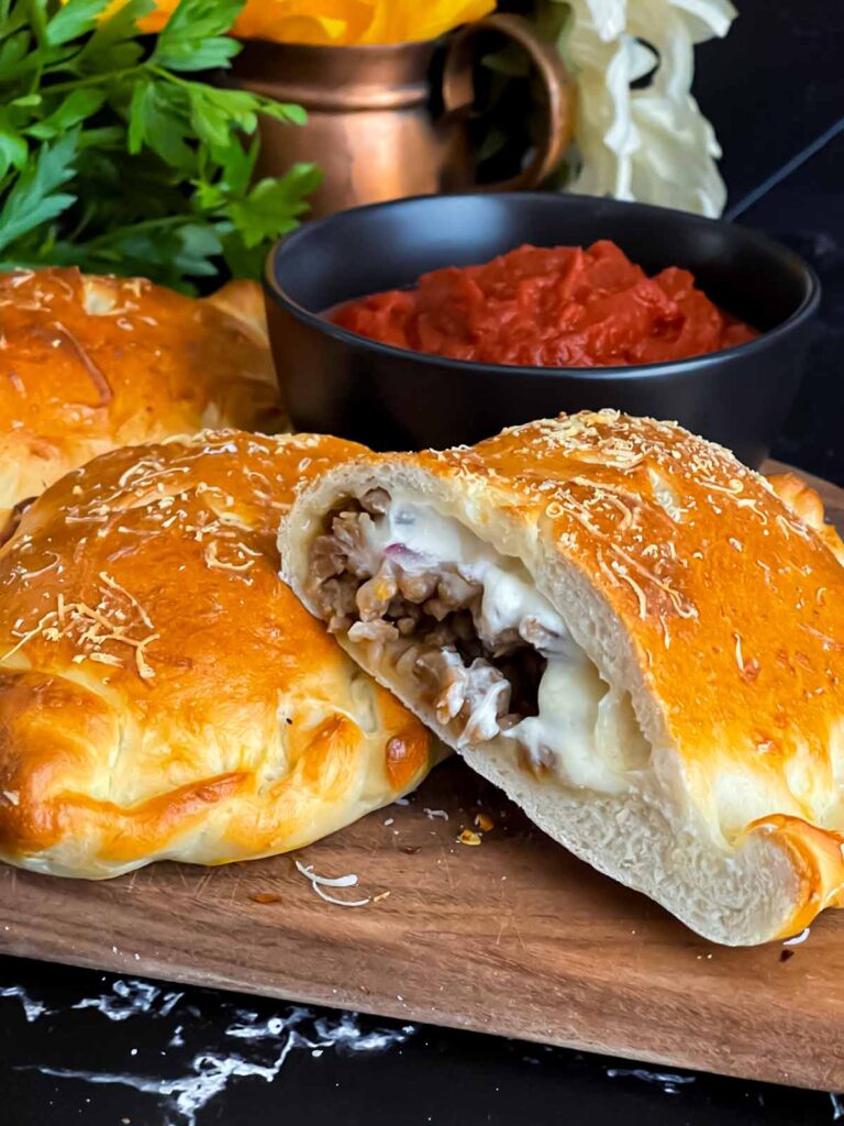 A calzone on a cutting board with a dipping sauce.