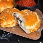 A calzone on a cutting board with a dipping sauce.