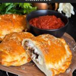 A calzone on a cutting board with a dipping sauce.