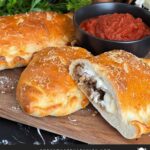 A calzone on a cutting board with a dipping sauce.