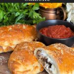 A calzone on a cutting board with a dipping sauce.