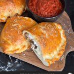 A calzone on a cutting board with a dipping sauce.