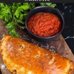 A calzone on a cutting board with a dipping sauce.