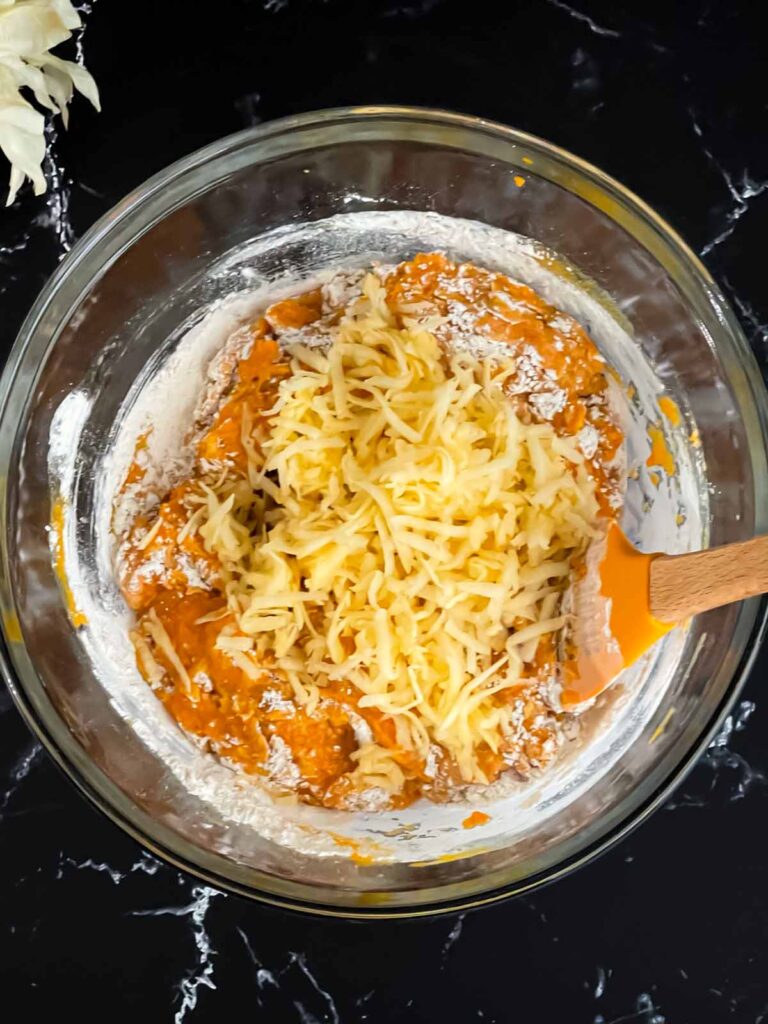 Shredded apple added to the pumpkin muffin batter in a glass mixing bowl.