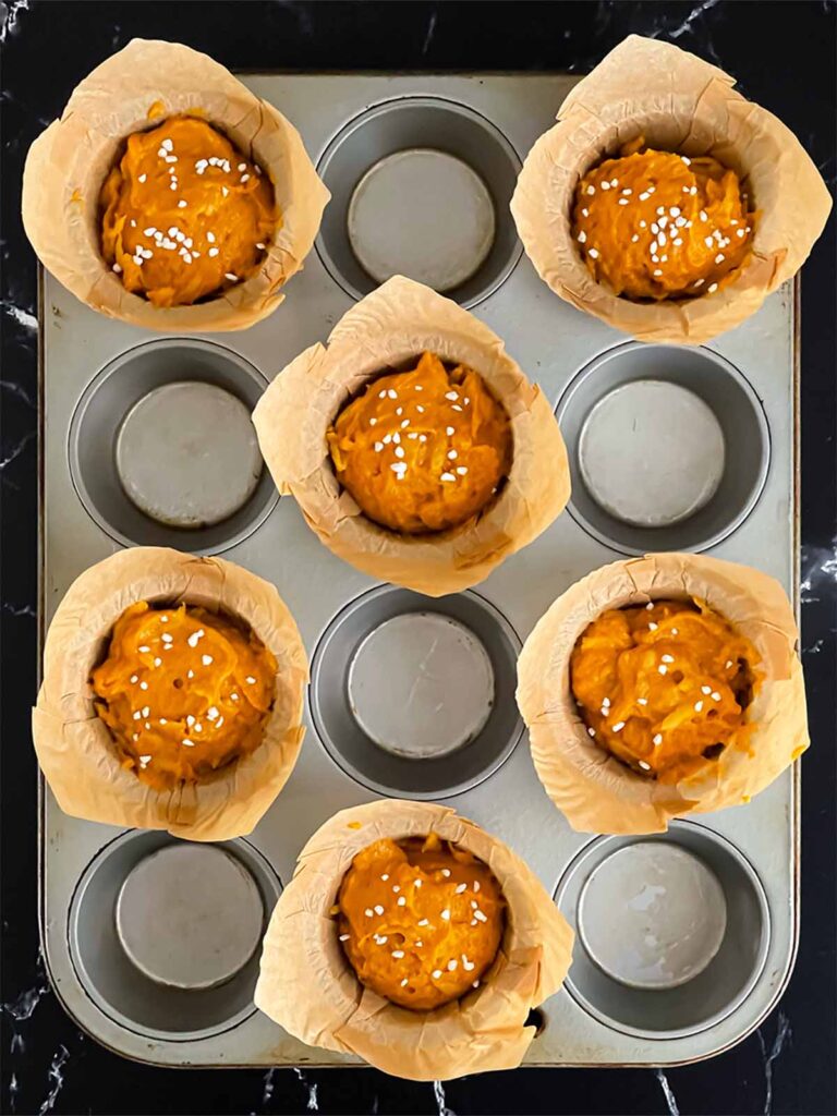 Pumpkin apple muffin batter divided into the paper lined muffin pan and sprinkled with pearl sugar.