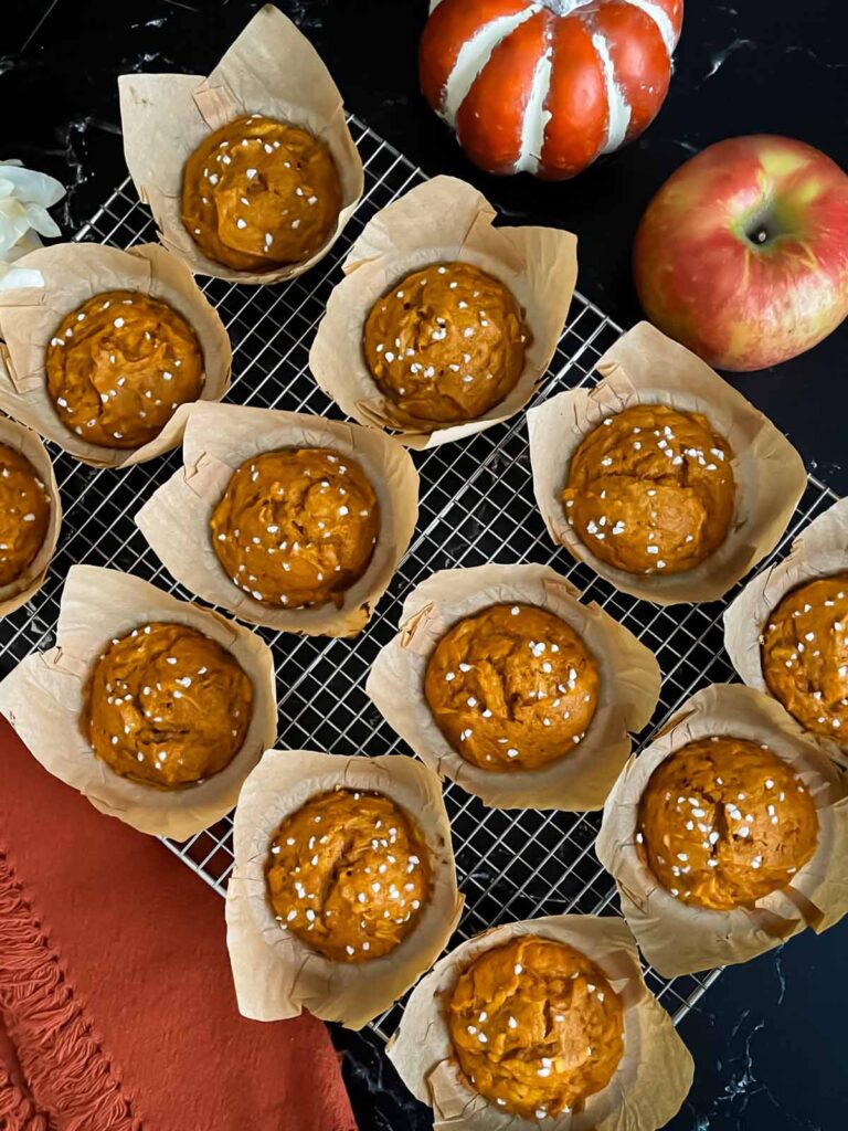 Pumpkin apple muffins on a wire rack on a dark surface.