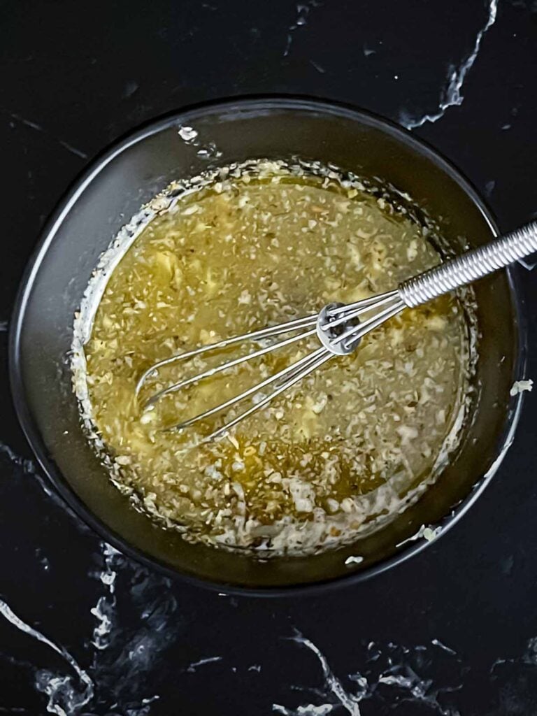 Slow cooker garlic parmesan potatoes herb butter mixture in a dark bowl on a dark surface.