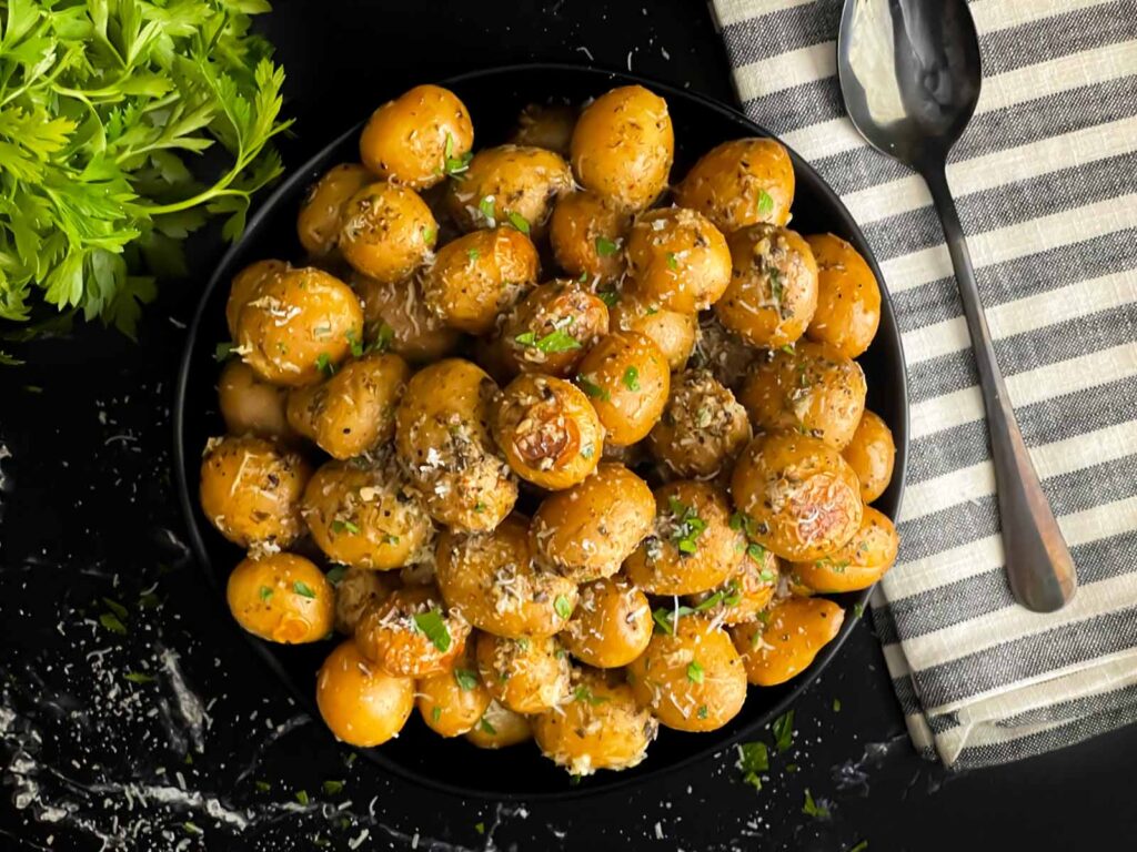 Slow cooker garlic parmesan potatoes in a dark bowl garnished with parsley and parmesan cheese.