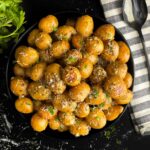 Slow cooker garlic parmesan potatoes in a dark bowl garnished with parsley and parmesan cheese.