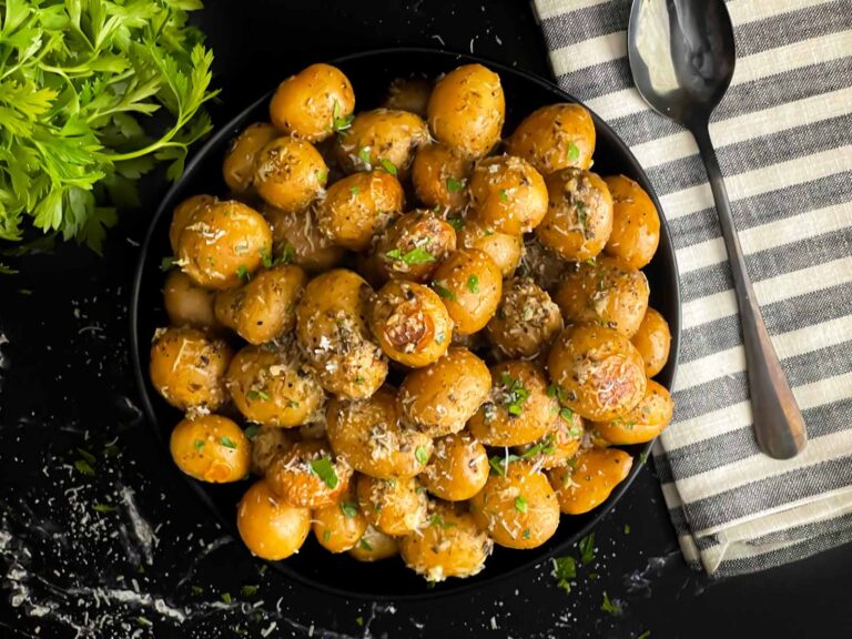 Slow cooker garlic parmesan potatoes in a dark bowl garnished with parsley and parmesan cheese.