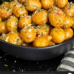 Slow cooker garlic parmesan potatoes in a dark bowl garnished with parsley and parmesan cheese.