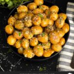 Slow cooker garlic parmesan potatoes in a dark bowl garnished with parsley and parmesan cheese.