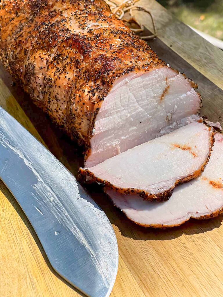 A Texas style smoked pork loin on cutting board with some slices.