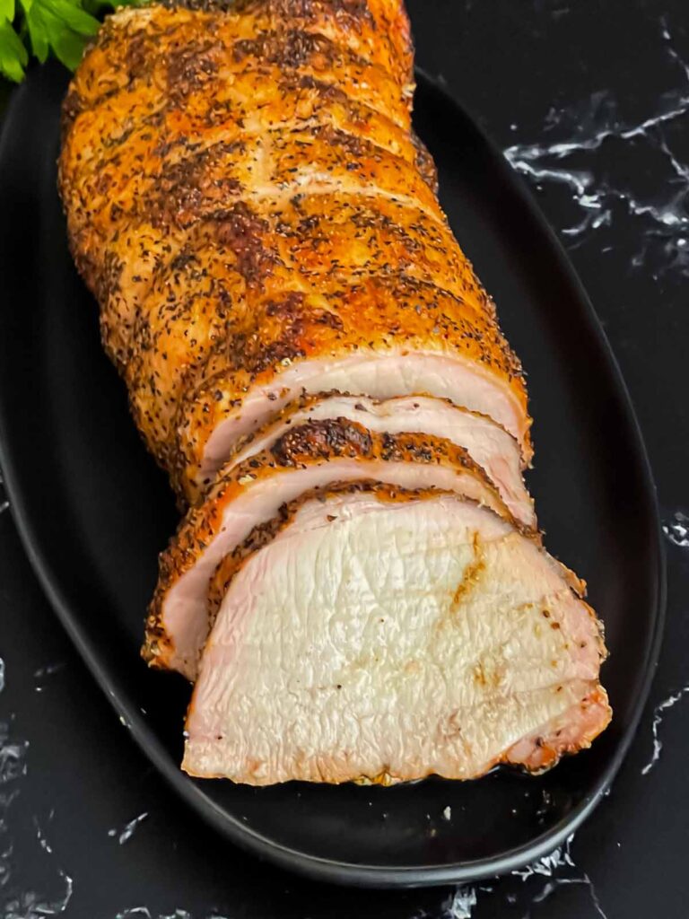 A Texas style smoked pork loin on a black serving plate with some slices.