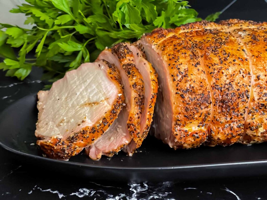 A Texas style smoked pork loin on a black serving plate.