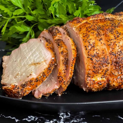 A Texas style smoked pork loin on a black serving plate.