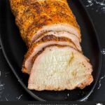 A Texas style smoked pork loin on black serving plate.