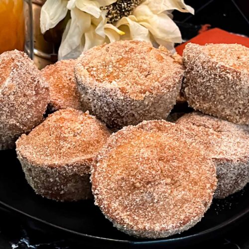 Apple cider muffins stacked on a dark plate on a dark surface.