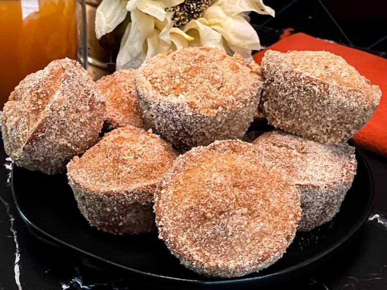 Apple cider muffins stacked on a dark plate on a dark surface.