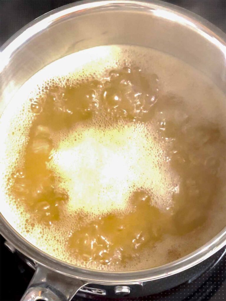 Apple cider boiling in a small sauce pan.