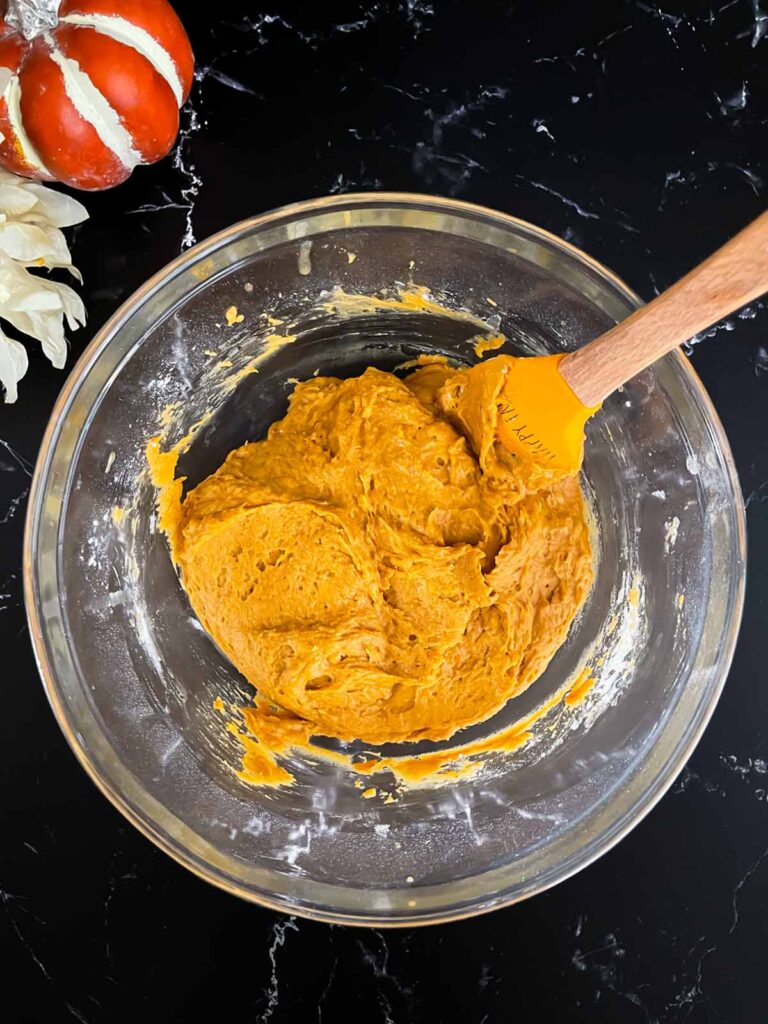 Baked pumpkin donuts batter mixed in a glass bowl on a dark surface.