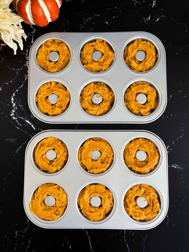 Baked pumpkin donut batter divided into donut pans on a dark surface.