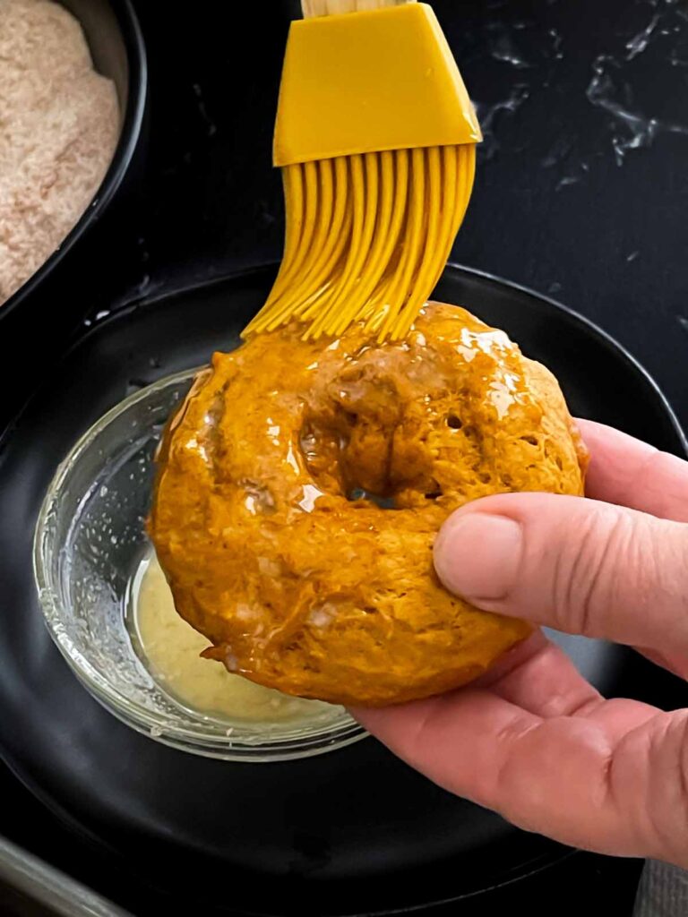 Melted butter being brushed onto a baked pumpkin donut.