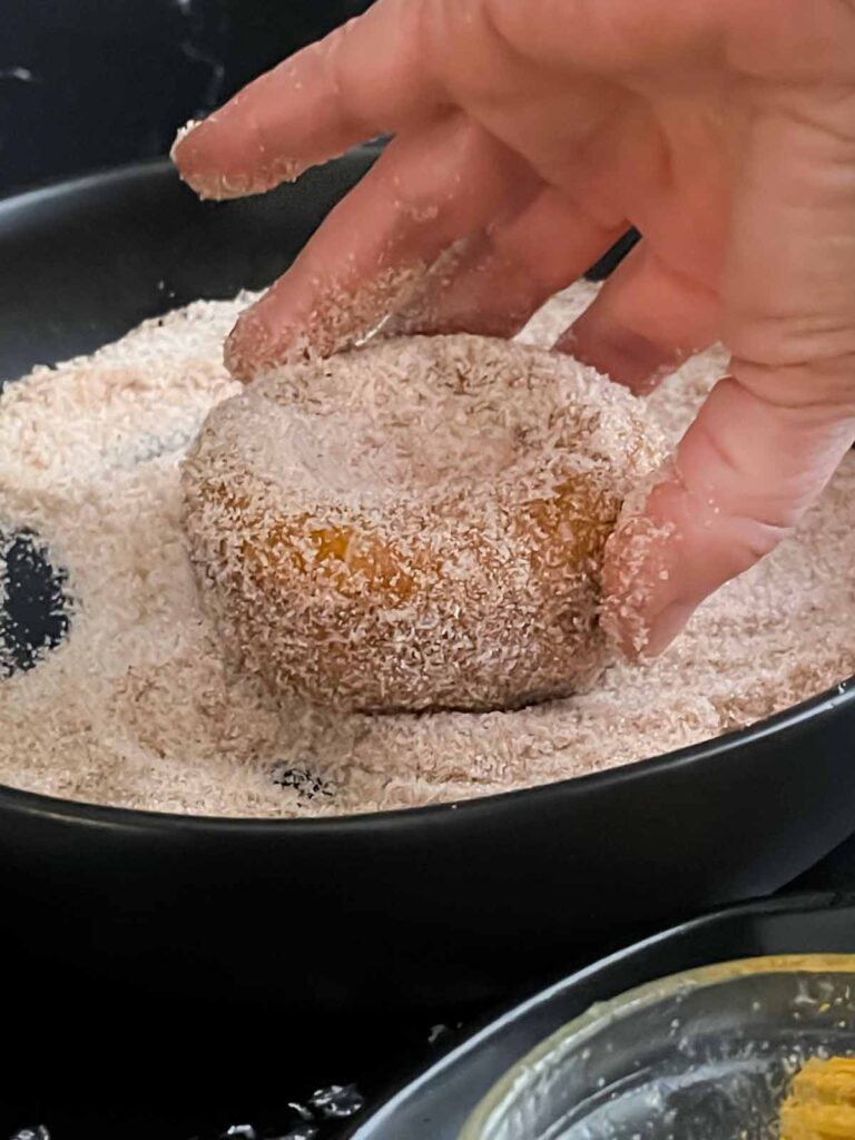 Baked pumpkin donut being rolled in the cinnamon sugar mixture.