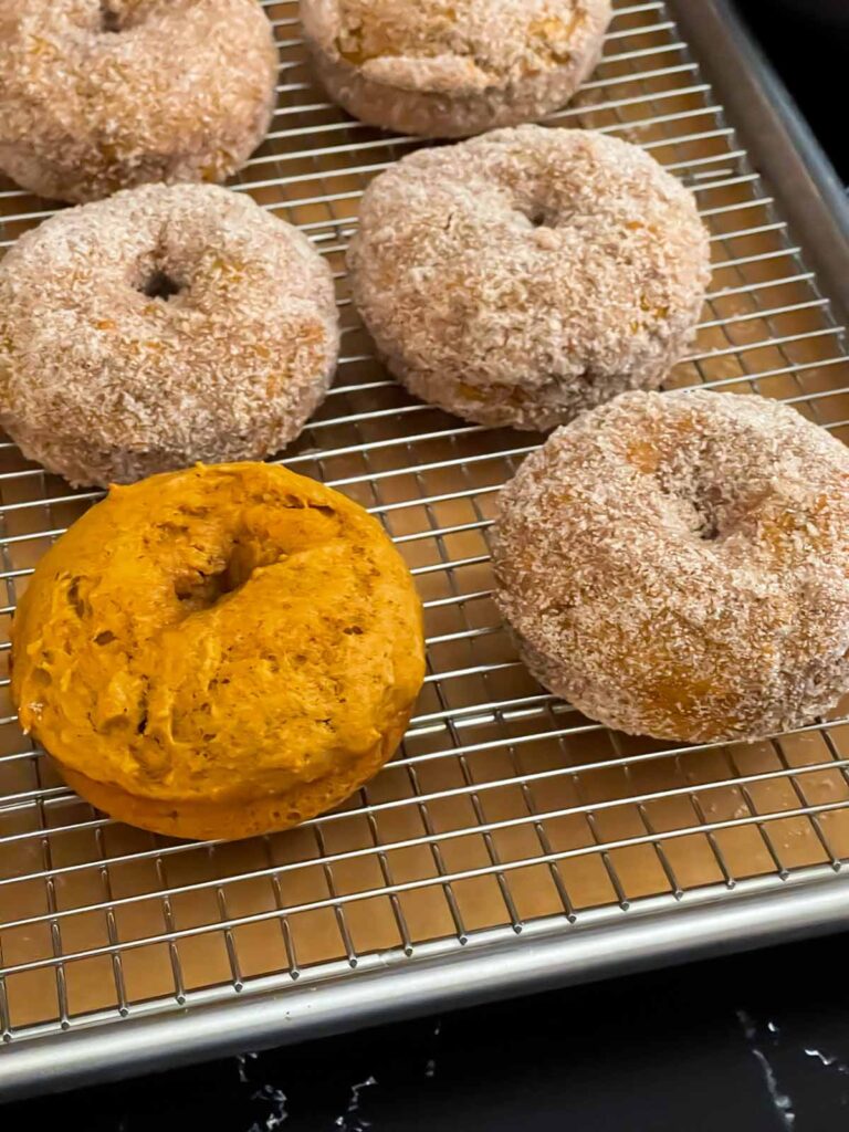 Baked pumpkin donuts rolled in cinnamon sugar on a wire rack over a parchment paper lined baking sheet.