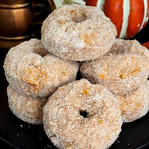 Baked pumpkin donuts stacked on a dark plate.