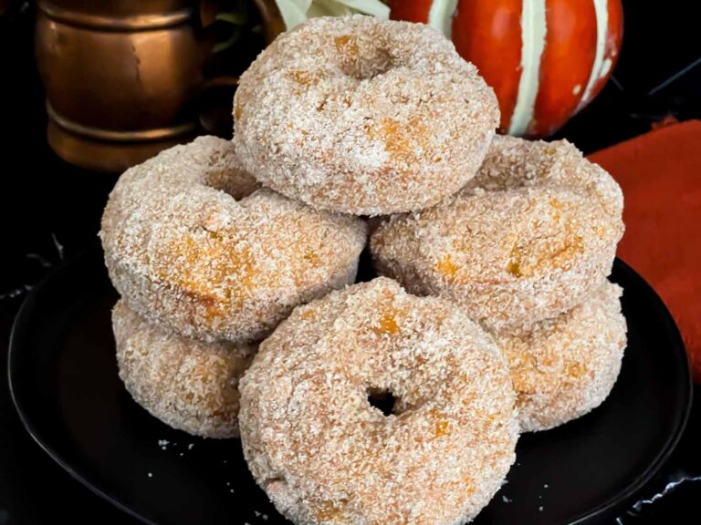 Baked pumpkin donuts stacked on a dark plate.