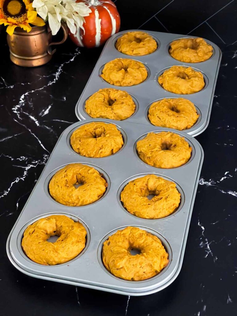 Baked pumpkin donuts in the donut pans on a dark surface.