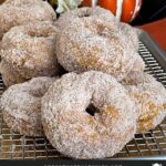 Baked pumpkin donuts stacked on a wire rack over a parchment paper lined baking sheet.