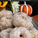 Baked pumpkin donuts stacked on a wire rack over a parchment paper lined baking sheet.