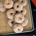 Baked pumpkin donuts stacked on a wire rack over a parchment paper lined baking sheet.