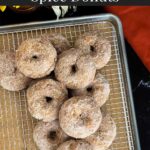 Baked pumpkin donuts stacked on a wire rack over a parchment paper lined baking sheet.