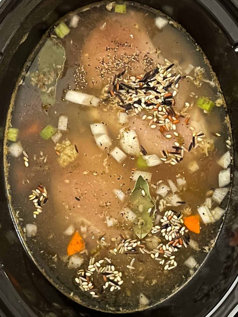 Slow cooker chicken and wild rice soup ingredients in the crock of a slow cooker.