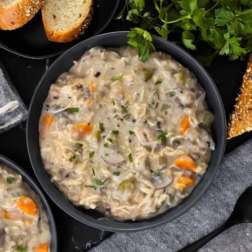 Slow cooker chicken and wild rice soup in a dark bowl with a cut loaf of crusty bread.