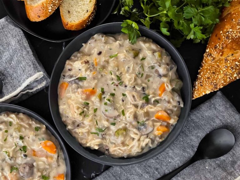 Slow cooker chicken and wild rice soup in a dark bowl with a cut loaf of crusty bread.