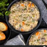 Slow cooker chicken and wild rice soup in a dark bowl with a cut loaf of crusty bread.