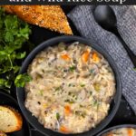 Slow cooker chicken and wild rice soup in a dark bowl with a cut loaf of crusty bread.