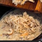 Shredded chicken being added back to the slow cooker chicken and wild rice soup.