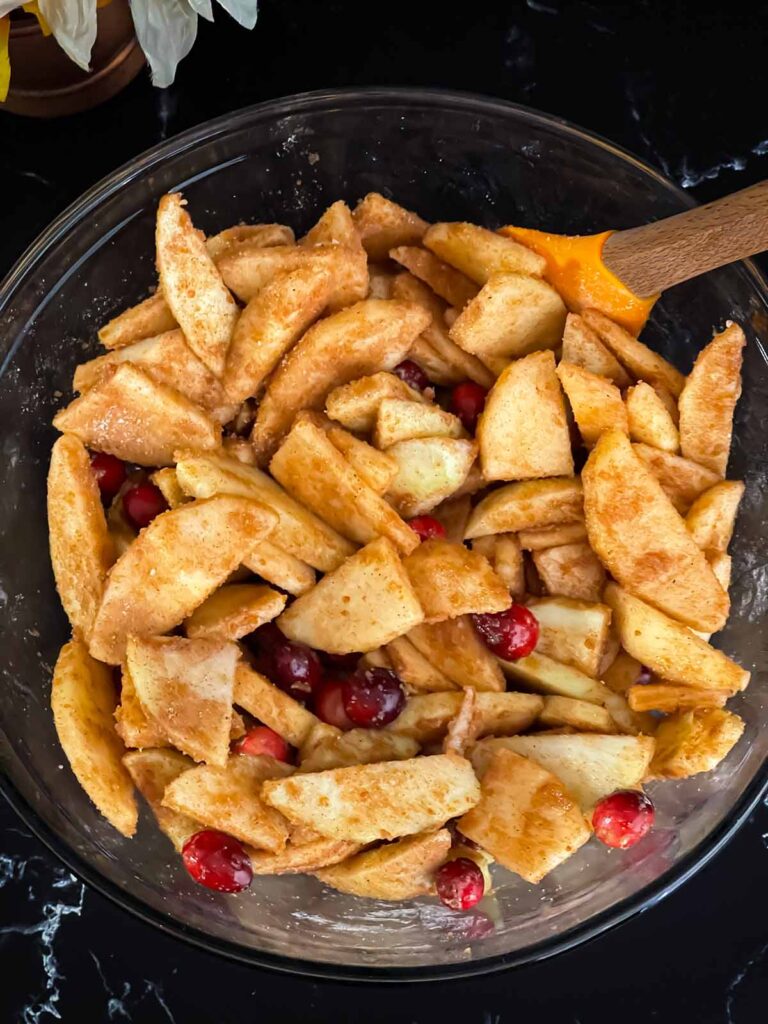 Sliced apples and cranberries coated in a cinnamon sugar mixture for the filling of the cranberry apple pie recipe.