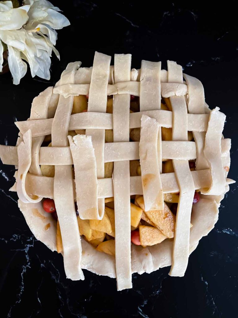 Pie dough in a lattice pattern on top of the cranberry apple pie filling.