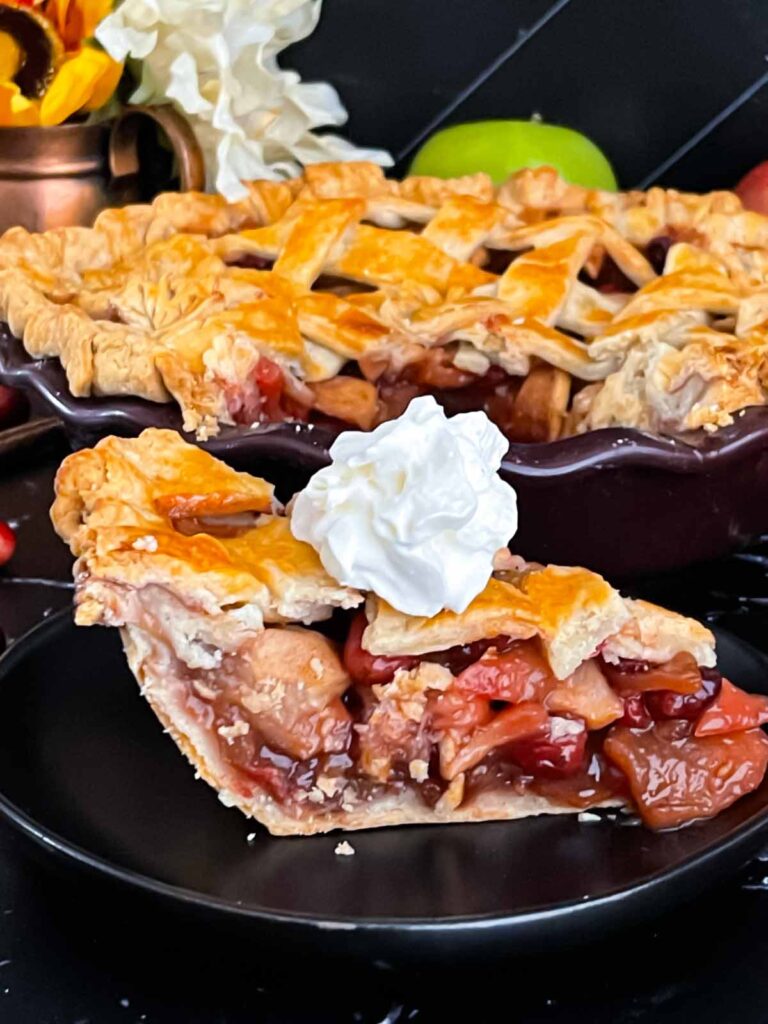 Slice of cranberry apple pie garnished with a dollop of whipped cream on a dark plate.