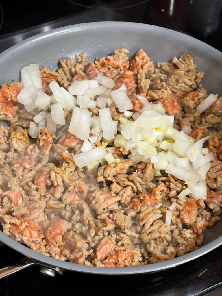 Onions added to Italian sausage in a skillet.