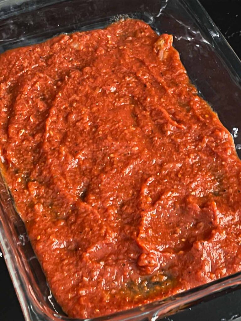 Marinara sauce spread in a 9x13 inch casserole dish.